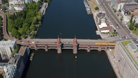 Aerial-view-of-U-bahn-train-crossing-historic-Oberbaum-bridge.-Old-double-deck-bridge-with-towers-next-to-road-bridge.-Berlin,-Germany