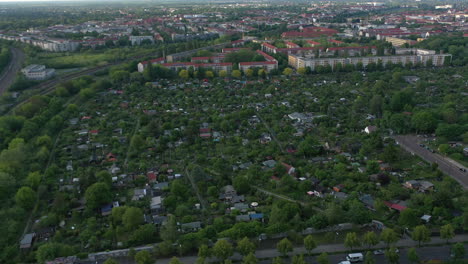 Fly-above-community-gardens-surrounded-by-railway-tracks-and-rows-of-residential-buildings.-Aerial-view-of-small-houses-in-green-vegetation.-Berlin,-Germany