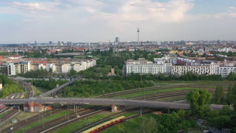 Backwards-reveal-of-multi-track-railway-line-dividing-into-directions,-railway-junction.-Panoramic-view-of-city-with-Fernsehturm.-Berlin,-Germany