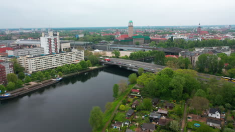 Fly-along-Havel-river-flowing-through-Spandau-borough.-Elevated-view-of-transport-infrastructure-and-buildings-in-city.-Berlin,-Germany
