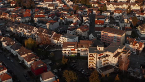 Forward-flying-drone-over-streets-with-family-houses-in-urban-neighbourhood.-White-house-facades-lit-by-bright-evening-sun.-Aerial-view.-Bad-Vilbel,-Germany.