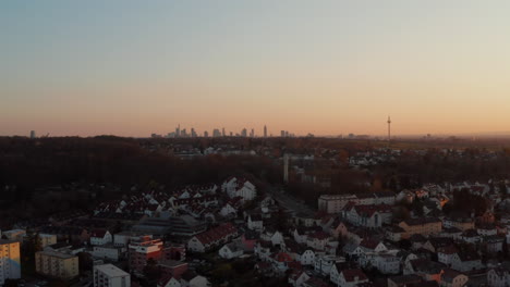 Distant-Frankfurt-am-Main-skyline-against-twilight-sky.-Descending-drone-footage-revealing-houses-and-streets-in-small-spa-town.-Bad-Vilbel,-Germany.