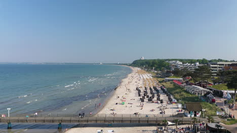 Scharbeutz-beautiful-aerial-view-of-shoreline-beach-with-people-sunbathing-enjoying-Baltic-sea,-forward,-Germany,-sunny-day