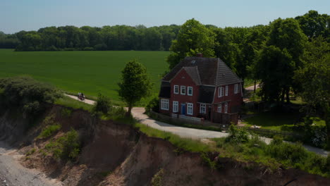 Aerial-drone-circling-around-beautiful-wooden-red-house-facing-Baltic-sea-in-Brodten,-Germany,-drone-flying-backwards-reveal-majestic-coastline-scenery,-day
