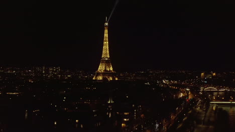 Eiffel-Tower-and-Seine-river-at-night.-Aerial-footage-of-illuminated-landmark-and-surrounding-town-development.-Paris,-France