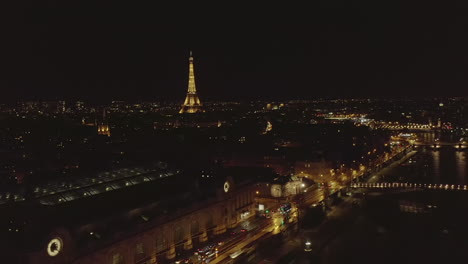 Aerial-view-of-night-city.-Revealing-Museum-Orsay-building-near-Seine-river,-Illuminated-Eiffel-Tower-in-distance.-Paris,-France