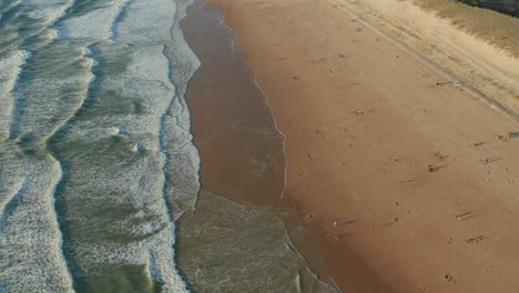 Few-People-Enjoying-Time-at-Beach-in-France-at-Golden-Hour-Sunset,-Aerial-low-angle-circling-slow