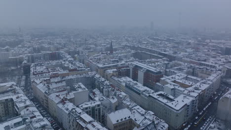 Fly-above-buildings-in-city.-Snowy-apartment-houses-along-streets-in-urban-neighbourhood.-Berlin,-Germany