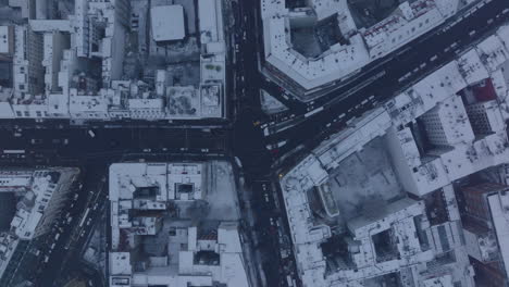 Aerial-birds-eye-overhead-top-down-ascending-view-of-street-intersection-in-winter-city.-Snow-dusted-roofs.-Berlin,-Germany