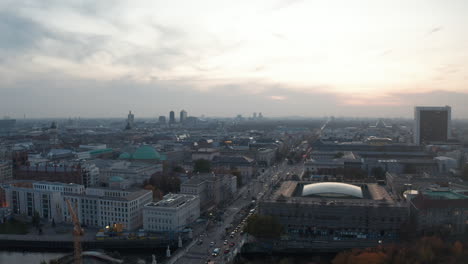 Ascending-panoramic-aerial-footage-of-large-town-at-dusk.-Traffic-on-long-straight-street.-Berlin,-Germany