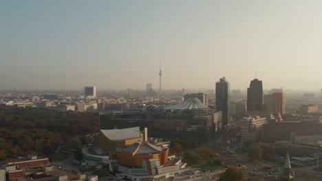 Aerial-panoramic-view-of-city-lit-by-bright-morning-sun.-Forwards-fly-above-Berlin-Philharmonic-buildings.-Fernsehturm-TV-tower-in-distance.-Berlin,-Germany
