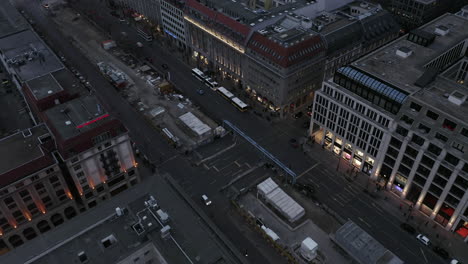 Ascending-aerial-footage-of-wide-boulevard-with-construction-site-in-middle.-Shopping-street-at-dusk.-Berlin,-Germany