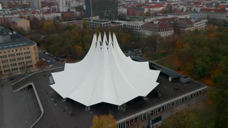 Futuristic-Modern-looking-Building-in-Berlin,-Germany-Tempodrom-white-Tent-in-Big-Cityscape,-Aerial-Dolly-forward
