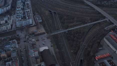 Aerial-slow-motion-view-of-empty-rail-lines-with-people-walking-on-foot-over-bridge-near-residential-houses-and-vehicles-parked-at-early-rise-morning-in-Berlin,-Germany