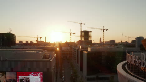 Passing-Mercedes-Benz-Arena-in-Berlin,-Germany-at-beautiful-Sunset-Golden-Hour-with-Alexanderplatz-TV-Tower-and-Sunflairs,-Aerial-Wide-Dolly-in,-circa-2019