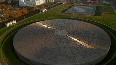 Modern-futuristic-flat-Building-architecture,-Velodrome-Arena-in-Berlin,-Germany-with-Sun-reflection-on-Metal-rooftop,-Aerial-tilt-down-birds-eye-view