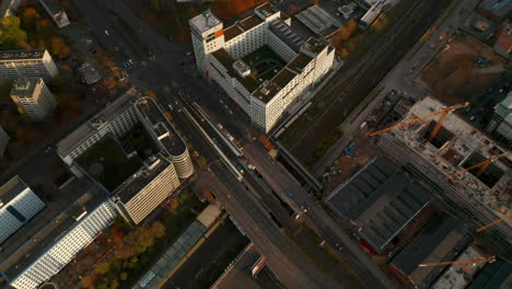 Train-passing-through-a-large-German-City-under-Bridge-with-Car-traffic-and-construction-site,-Aerial-Birds-Eye-Overhead-Top-Down-View