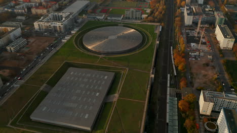 Establecimiento-De-Una-Toma-Aérea-Sobre-El-Estadio-De-Ciclismo-Futurista-Del-Edificio-Del-Velódromo-En-Berlín,-Alemania,-Vista-Aérea-Inclinada-Hacia-Arriba-Al-Atardecer