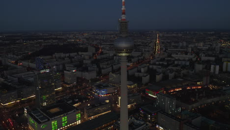 Aufsteigender-Blick-Auf-Den-Berliner-Fernsehturm-Alexanderplatz-Bei-Nacht-Mit-Stadtbild-Und-Licht-Im-Hintergrund,-Luftdrohnenkran-Hochgeschossen