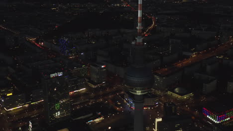 Vista-De-Cerca-Del-Rascacielos-De-La-Torre-De-Televisión-De-Berlín-Por-La-Noche-Con-El-Paisaje-Urbano-Alemán-En-La-Distancia,-Creador-Aéreo