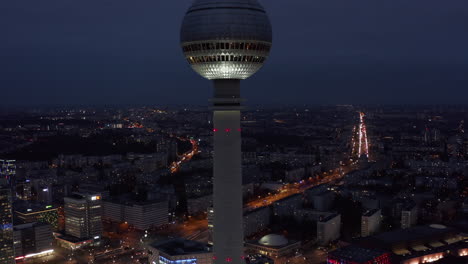 Bajando-Lentamente-La-Vista-Aérea-Amplia-Del-Rascacielos-De-La-Torre-De-Televisión-Con-El-Paisaje-Urbano-Por-La-Noche-En-Berlín,-Alemania,-Perspectiva-De-Drones-Desde-Arriba