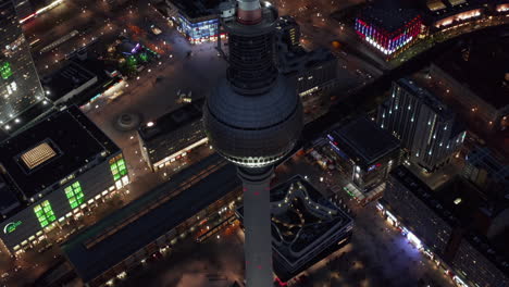 Famous-Berlin-TV-Tower-Skyscraper-above-Cityscape-at-Night-with-colorful-lights-in-German-Capital-City,-Aerial-Wide-Establishing-Shot-backwards-dolly-out