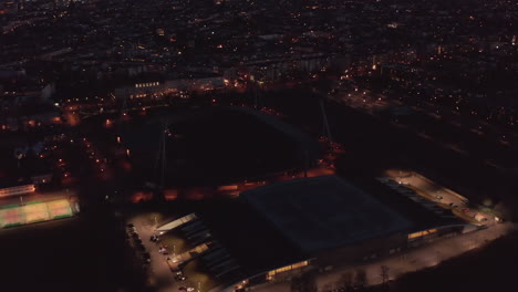 Incline-Hacia-Arriba-Para-Revelar-El-Panorama-Nocturno-De-La-Ciudad-Con-La-Torre-De-Vigilancia-De-La-Televisión,-Fernsehturm.-Antena-Con-Zona-Deportiva-Y-Calles-Aledañas.-Berlín,-Alemania.