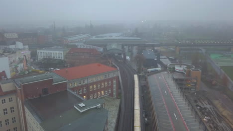 Aerial-follow-Shot-of-Yellow-Subway-Train-in-Berlin-in-Foggy-Cityscape-on-Train-Tracks,-Foggy-weather-with-clouds,-Drone-Shot