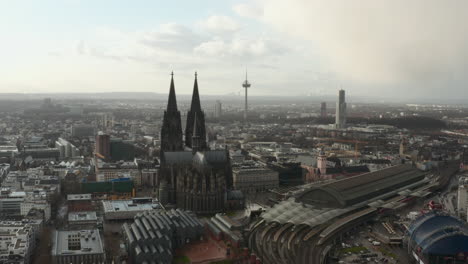 Slide-and-pan-aerial-footage-of-Cathedral-Church-of-Saint-Peter,-train-station-and-surrounding-buildings.-Cologne,-Germany