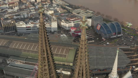Aerial-ascending-footage-of-top-of-cathedral-tower.-Tilt-down-revealing-large-buildings-in-main-train-station.-Cologne,-Germany