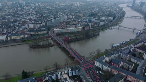 Aerial-panoramic-footage-of-wide-river-flowing-through-city.-Slide-and-pan-shot-of-traffic-on-old-road-bridge.-Church-on-waterfront.-Frankfurt-am-Main,-Germany