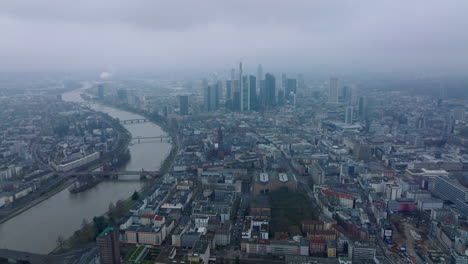 Aerial-panoramic-footage-of-large-city-on-hazy-day.-Wide-river-flowing-through-city.-Group-of-modern-downtown-skyscrapers.-Frankfurt-am-Main,-Germany