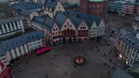 High-angle-view-of-historic-square.-Fountain-and-medieval-houses-around-Roemerberg.-Tilt-up-reveal-of-group-of-modern-downtown-skyscrapers.-Frankfurt-am-Main,-Germany
