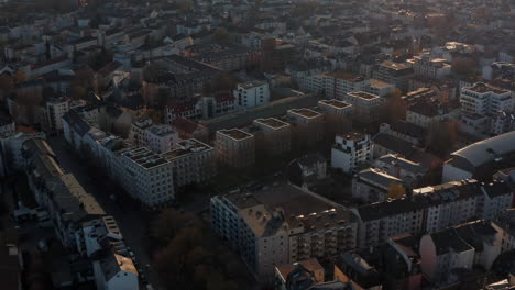 Aerial-view-from-drone-flying-above-urban-neighbourhood-in-golden-hour.-Tilt-up-footage-revealing-skyline-with-group-of-skyscrapers-against-sun.-Frankfurt-am-Main,-Germany