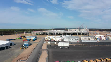 Slow-flight-dolly-forward-above-huge-Factory-construction-site-in-rural-landscape-of-Germany,-Gigafactory-Berlin,-Aerial-Wide-Angle-Shot