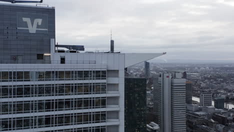 Tight-fly-above-top-of-DZ-Bank-skyscraper.-Revealing-panoramic-view-of-city-with-tall-office-buildings.-Frankfurt-am-Main,-Germany