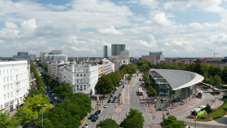 Forwards-fly-above-street-lined-with-green-lead-trees.-Flying-along-modern-designed-public-transport-terminal.-Free-and-Hanseatic-City-of-Hamburg,-Germany