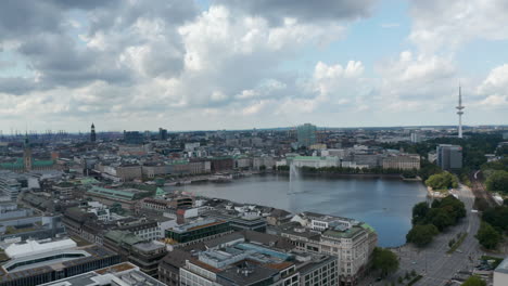Sliding-aerial-footage-of-water-surface-surrounded-by-buildings-and-with-fountain-in-middle.-Fly-along-Binnenalster-lake.-Free-and-Hanseatic-City-of-Hamburg,-Germany