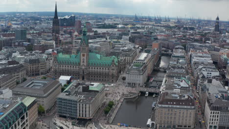 Fly-above-historic-city-centre-with-city-hall-building-and-churches.-Harbour-cranes-in-background.-Free-and-Hanseatic-City-of-Hamburg,-Germany