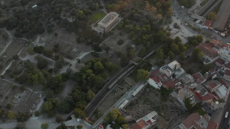 Aerial-View-of-Train-Passing-through-Athens,-Greece-by-Ancient-Ruins-and-Historic-City-Parts-in-Golden-Hour-Sunset-Light