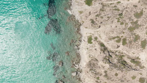 Overhead-Top-Down-Aerial-Flight-over-Greek-Island-Milos-Turquoise-Blue-Ocean-with-Rocky-Cliff-Coast