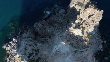 Top-Down-Luftbild-Der-Generischen-Bergküste-Mit-Türkisfarbenem-Wasser-Und-Wellen,-Die-Bei-Sonnenuntergang-Auf-Felsen-Auf-Der-Griechischen-Insel-Krachen