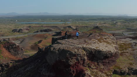 Drone-birds-eye-view-two-young-male-tourist-standing-on-top-of-cliff-in-Iceland.-Aerial-view-explorer-hikers-traveler-enjoying-calm-and-quiet-looking-panorama