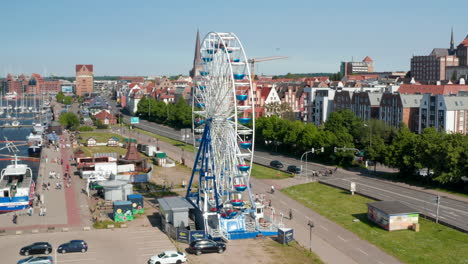Rising-view-of-running-Ferris-wheel.-People-enjoying-time-on-attraction.-Ascending-and-tilting-down-footage-with-city-in-background