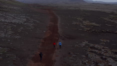 Aerial-view-three-traveler-adventurous-hikers-walking-pathway-in-desert-landscape-in-Iceland.-Drone-point-of-view-of-three-explorer-enjoying-healthy-lifestyle-in-isolated-highlands