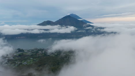 Slow-aerial-dolly-shot-flying-through-the-clouds-past-small-valleys-towards-lake-Batur-and-mount-Agung-in-Bali,-Indonesia