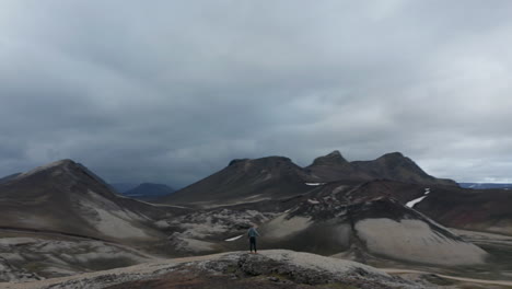 Drone-view-orbit-around-man-arms-open-standing-mountain-peak-feeling-free-admiring-skaftafell-national-park,-Iceland.-Aerial-view-adventurous-man-on-top-of-the-mountain-enjoying-the-beautiful-view
