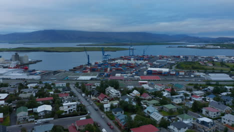 Forwards-fly-above-family-houses-in-urban-neighbourhood.-Stacks-of-naval-containers-and-huge-cranes-in-harbour.-Reykjavik,-Iceland