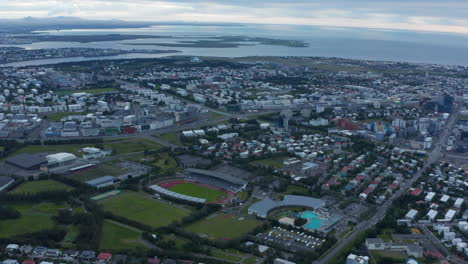 Aerial-panoramic-footage-of-town-at-dusk.-Sports-centres-and-residential-borough.-Sea-in-background.-Reykjavik,-Iceland