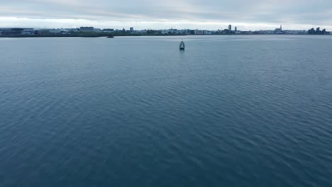 Tiefflug-über-Der-Wasseroberfläche.-Aufkippen-Der-Gebäude-In-Der-Stadt-Am-Ufer.-Bedeckter-Himmel.-Reykjavik,-Island